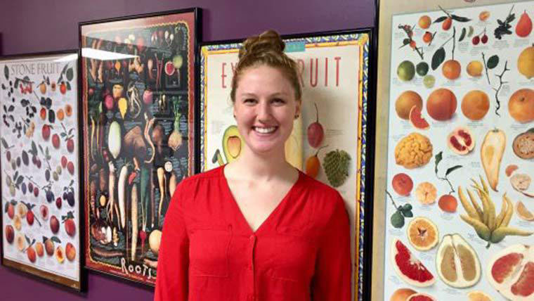 Student Dietetic Association member standing in front of fruit and vegetable posters.