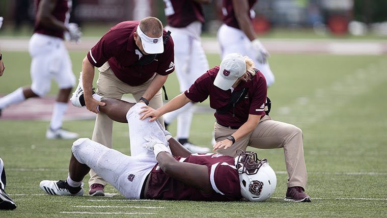Trainers examining potential injury to football player.