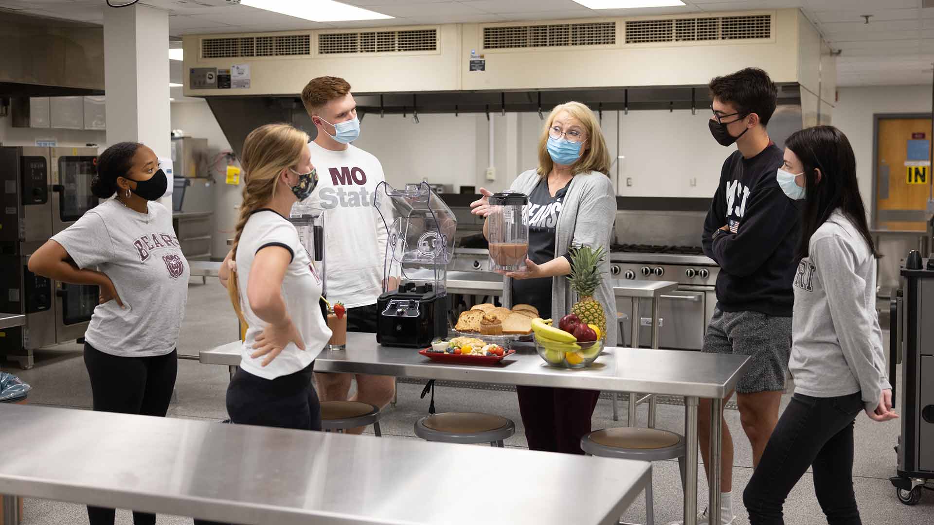 A dietetics professor speaking to a group of students in a kitchen lab in Kampeter.